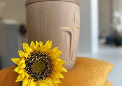 Urne aus Holz mit einem Kreuz geschmückt mit einer Sonnenblume
